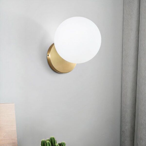 Tegen een witte achtergrond staat een gouden en witte wandlamp in de vorm van een verlichte glazen bol.