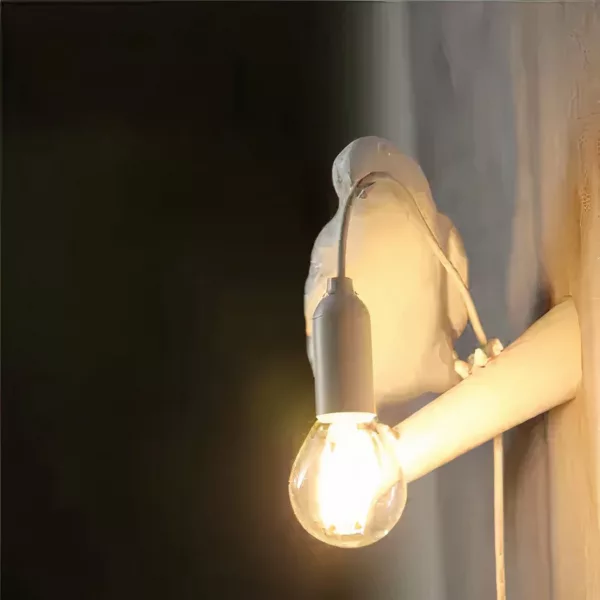 Een witte raafvormige wandlamp brandt tegen een zwarte achtergrond.