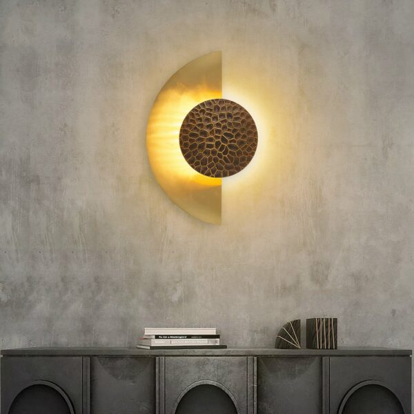 Op een donkergrijze muur hangt in het midden een wandlamp in de vorm van een verlichte gouden halve maan.