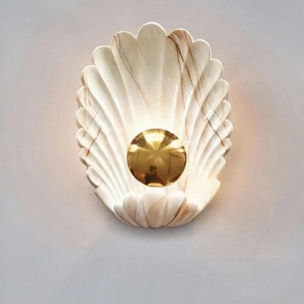 Een witte en gouden wandlamp in de vorm van een schelp tegen een witte achtergrond.