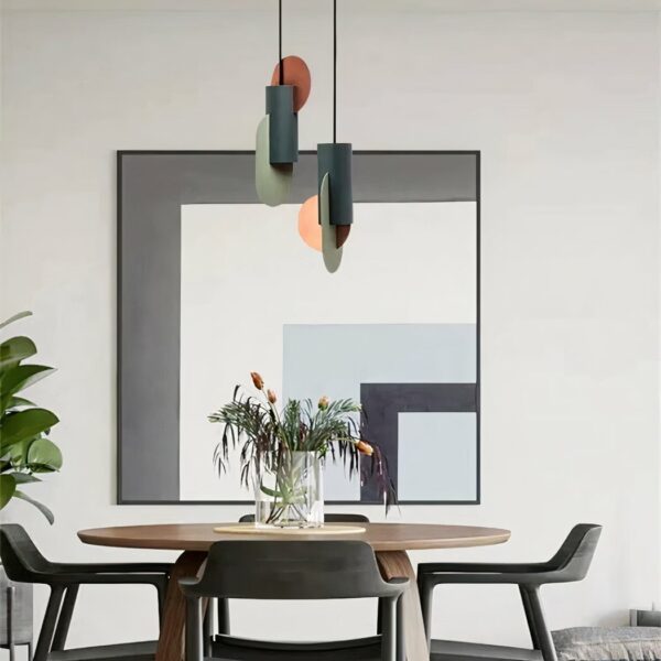 Moderne art-deco kroonluchters hangen boven een ronde tafel met een vaas bloemen. Er staan drie stoelen rond de tafel, een witte muur op de achtergrond en een groot L-vormig schilderij in grijs, wit, blauw en zwart.