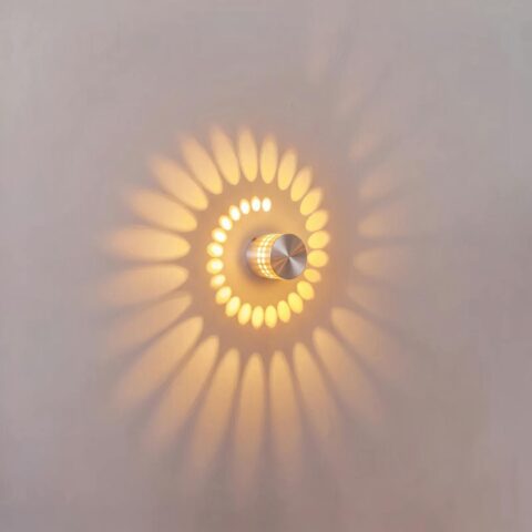 Ronde LED-wandlamp in aluminium met circulaire lichtprojectie Ronde led-wandlamp van zilverkleurig aluminium, aan, projecteert een spiraal van warm licht op een witte muur