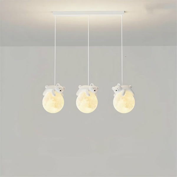 Hanglamp bestaande uit drie kabels, elk met een bal die de maan voorstelt en een teddybeer die op de maan slaapt. De ballen zijn verlicht. De rechthoekige basis hangt aan het lichtgrijze plafond, met een lichtgrijze muur op de achtergrond.