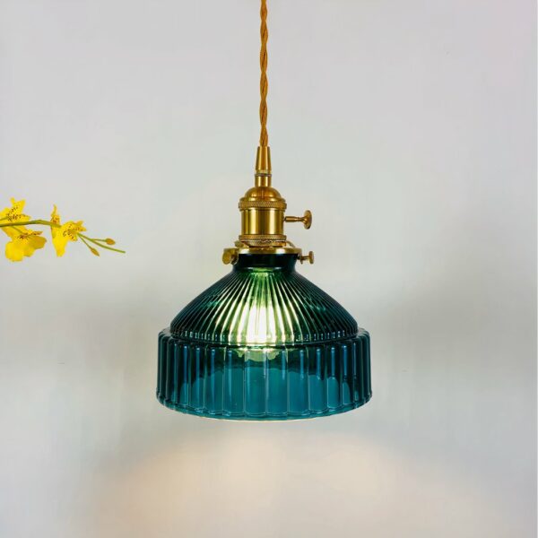 Vintage hanglamp met gedraaide gouden kabel en gouden lamphouder, eendenblauwe kap die op een bel lijkt met ribbels rondom. Lamp brandt. Gele bloemen links.