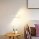Witte diagonale LED-wandlamp boven een rond bijzettafeltje naast de bank